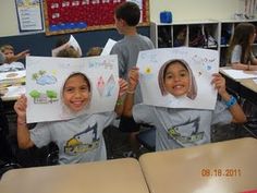 two children holding up pictures of themselves in the classroom