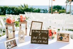 a table with pictures and flowers on it at an outdoor wedding reception in front of the ocean