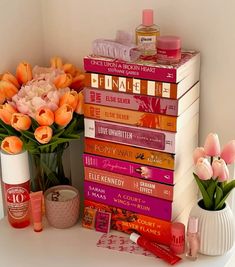 a stack of books sitting on top of a white table next to flowers and lipstick