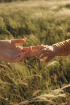 two people reaching out their hands to touch each other's hand in a field