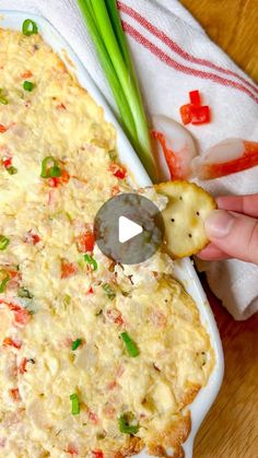 a person dipping some crackers into a casserole dish with green onions and red peppers