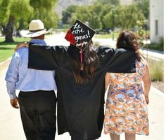 a man and woman walking down a sidewalk with their arms around each other wearing graduation caps