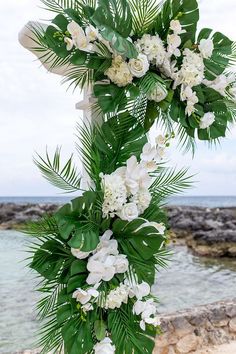 a wedding arch with white flowers and greenery on the beach by the water's edge