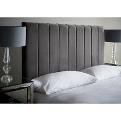 a bed with two lamps on either side of it and a gray headboard that has white pillows