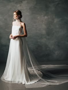 a woman in a white wedding dress is standing with her veil draped over her head