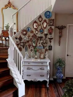 a white dresser sitting under a stair case next to a wall with plates on it