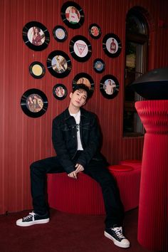 a young man sitting on top of a red bench in front of a wall covered with plates