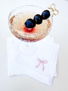 a small glass bowl filled with liquid and black olives on top of a white napkin