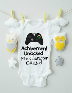 a baby bodysuit that says achievement unlocked, new character created and an owl hanging from clothes pins