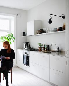 a woman sitting on a chair in a kitchen reading a magazine next to a window