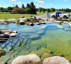 a truck is parked in the middle of a pond with rocks and grass around it