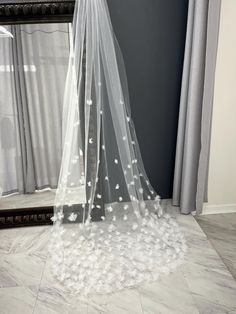 a white veil is hanging over a bed in front of a mirror with flowers on it