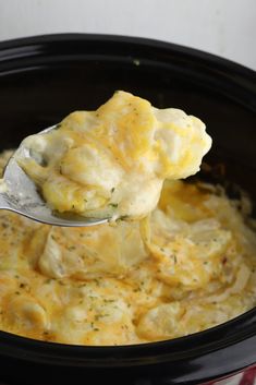 a spoon with some food in it on top of a crock pot filled with broccoli and cheese