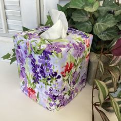 a tissue box covered in colorful flowers next to a potted plant