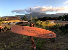 a woman holding a surfboard in front of her face with mountains in the background