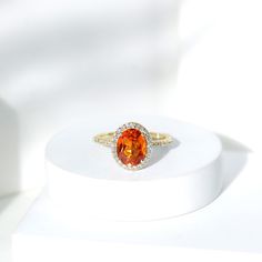 an orange and white diamond ring sitting on top of a white stand in front of a white background