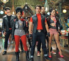 several people in costumes standing on a wooden floor with lights behind them and one person wearing black leather jacket