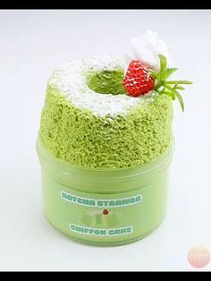 a green cake with white frosting and a strawberry on top in a small plastic container