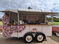 a food cart with flowers on the side and an old car parked in front of it