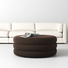 a white couch with a brown ottoman on top of it next to a white wall