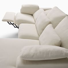 a large white couch with pillows on it's back and arm rests against the wall