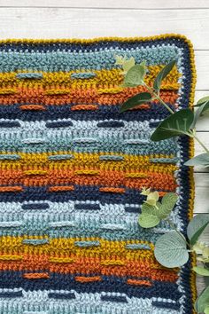 a crocheted placemat with leaves on the edge and an orange, blue, yellow and green stripe