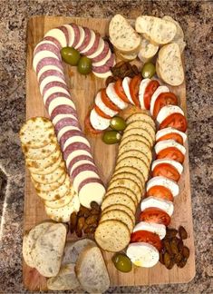 a wooden cutting board topped with different types of appetizers next to crackers and olives