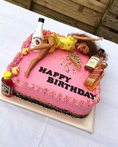 a birthday cake with a barbie doll laying on it and bottles of booze in the background