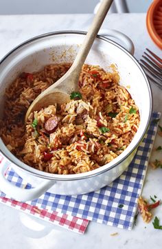 a pot filled with rice and sausage on top of a checkered cloth next to a wooden spoon