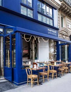 the outside of a blue restaurant with tables and chairs