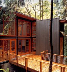 a wooden deck in front of a house surrounded by trees and woods with lots of windows