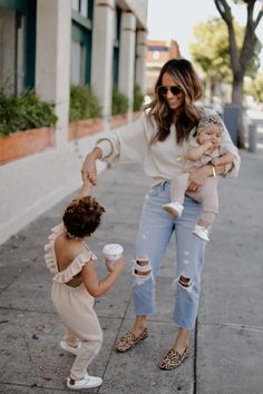 a woman holding a baby and two other women standing on the sidewalk with coffee in their hands