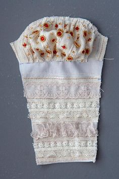 an old piece of cloth with lace and flowers on it is laying on a gray surface