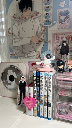 an assortment of toys and books on a desk with anime characters in the back ground