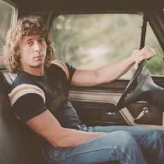 a man sitting in the driver's seat of a car holding a steering wheel