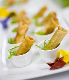 appetizers are arranged in small cups on a white tray with flowers and leaves