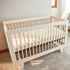 a white crib sitting on top of a carpeted floor next to a window