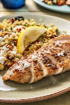 a white plate topped with chicken, rice and lemon wedges