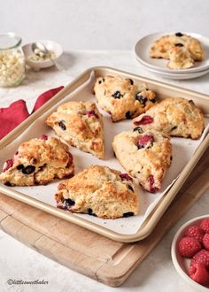 several scones on a tray with raspberries and other fruit in the background