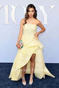 a woman in a yellow dress standing on a blue carpet with her hands on her hips