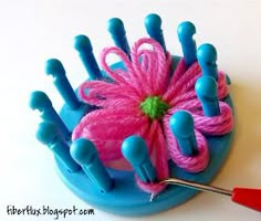 a pink flower sitting on top of a blue plate next to knitting needles and crochet hooks