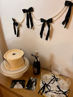 a table topped with a cake covered in white frosting and black ribbon decorations next to wine glasses