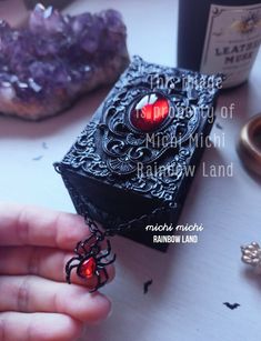 a hand holding a small black box with a red heart on it next to some other items