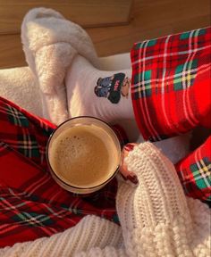 a person in red and green plaid pants holding a cup of hot chocolate next to their feet