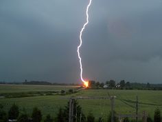 a lightning bolt hitting through the sky over a field