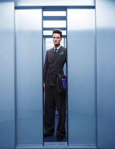 a man standing in an elevator wearing a suit and holding a blue bag with his hand