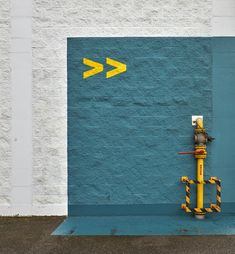 a yellow fire hydrant in front of a blue wall with an arrow painted on it