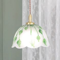 a green and white light hanging from a ceiling fixture in front of a curtained window