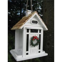 a white birdhouse with a wreath hanging from it's roof and a red bow on the door