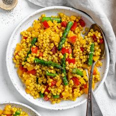 two plates filled with corn and vegetables on top of a white table next to silverware